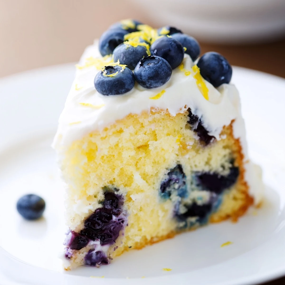 Homemade Lemon Blueberry Cake with Cream Cheese frosting on a wooden board, topped with plump blueberries and bright lemon zest curls.