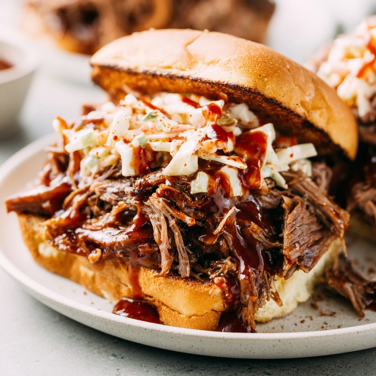 Glossy barbecue-coated Slow Cooker Pulled Beef Sandwiches piled high on soft buns, ready to serve with pickles.