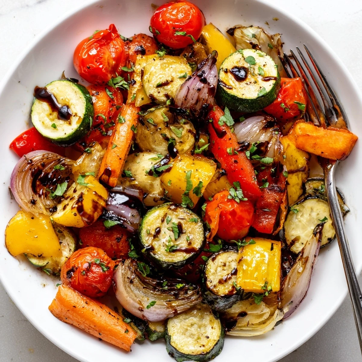 Colorful roasted vegetable mix in a white bowl, garnished with fresh parsley and a drizzle of balsamic vinegar.