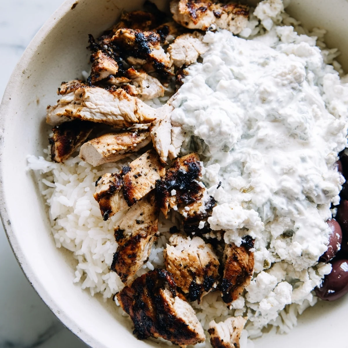 Freshly grilled marinated chicken slices rest on fluffy rice, topped with feta, olives, and creamy tzatziki in Greek Chicken Gyro Bowls.