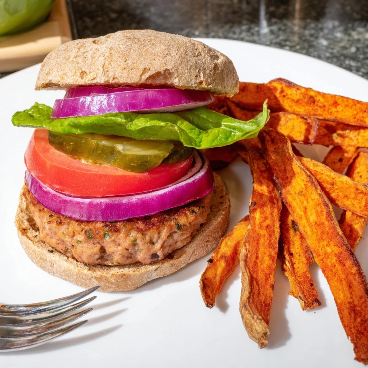 Close-up view of a perfectly cooked turkey patty with fresh lettuce, tomato, and onion, served alongside sweet potato fries.  