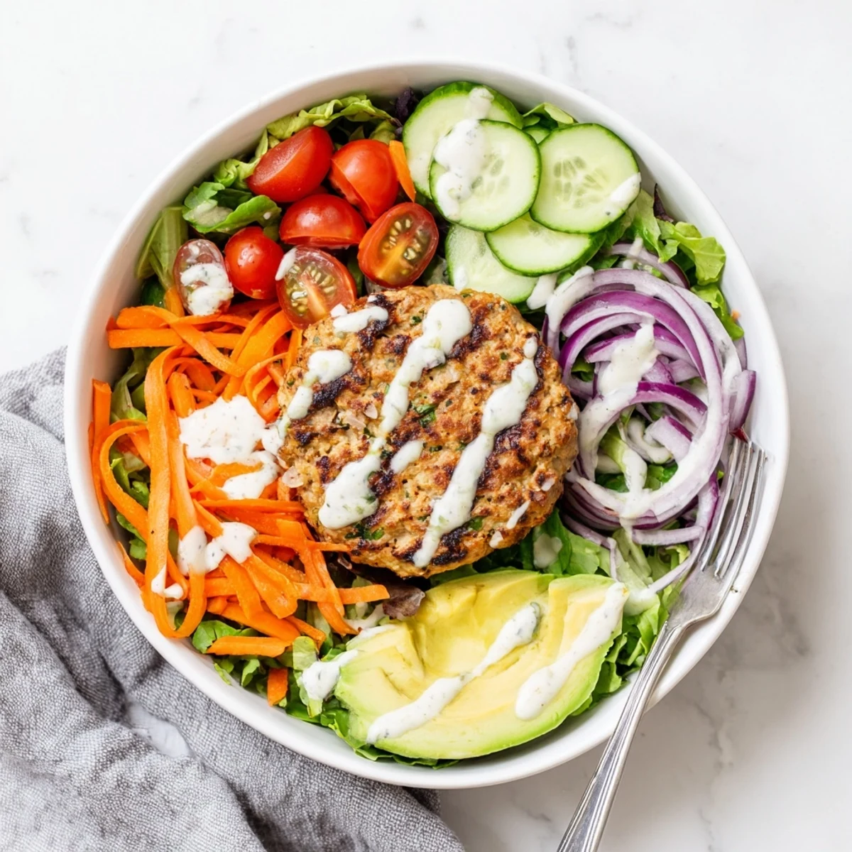 Golden-brown turkey burger patties rest atop a vibrant salad bowl of mixed greens, cherry tomatoes, cucumber, and creamy avocado slices.