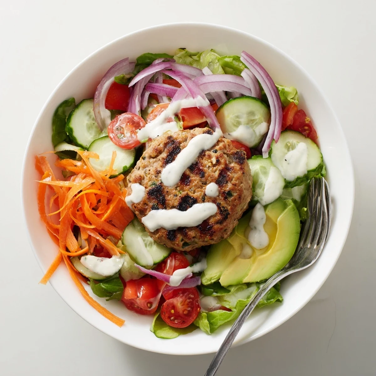 Savory ground turkey burger served as a hearty salad bowl with crisp veggies and a drizzle of tangy yogurt dressing.