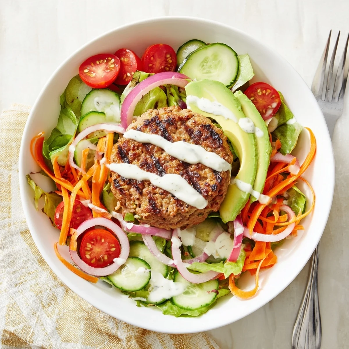 Fresh gluten-free salad bowl featuring juicy turkey burger patty, julienned carrots, red onion, and dill-flecked yogurt dressing ready to eat.