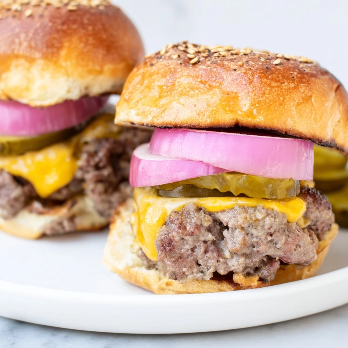 Golden-brown Tailgate Burger Sliders with Pickles on a platter, with melted cheddar and fresh red onion.