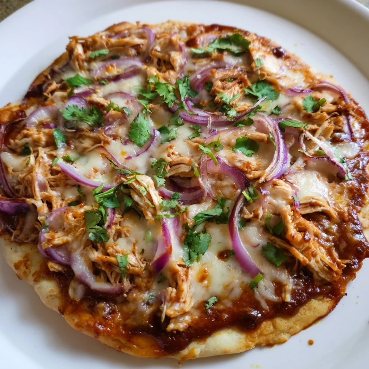 Golden crust on a homemade BBQ Chicken Pizza with Red Onion, showcasing tangy sauce and bubbly, stretchy cheese.