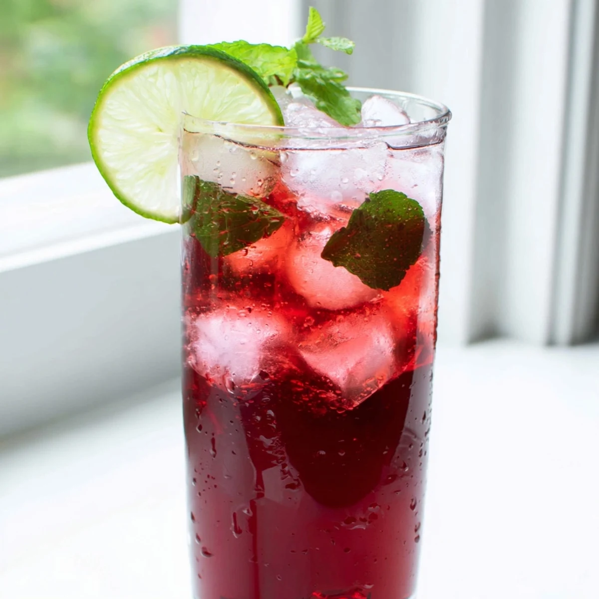 A close-up of Hibiscus Iced Tea with Lime served over ice, garnished with fresh mint and vibrant lime wheels.  