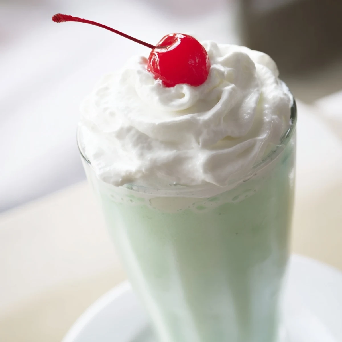 Refreshing mint milkshake with whipped cream and a maraschino cherry, poured into two glasses for a sweet, cool beverage treat.