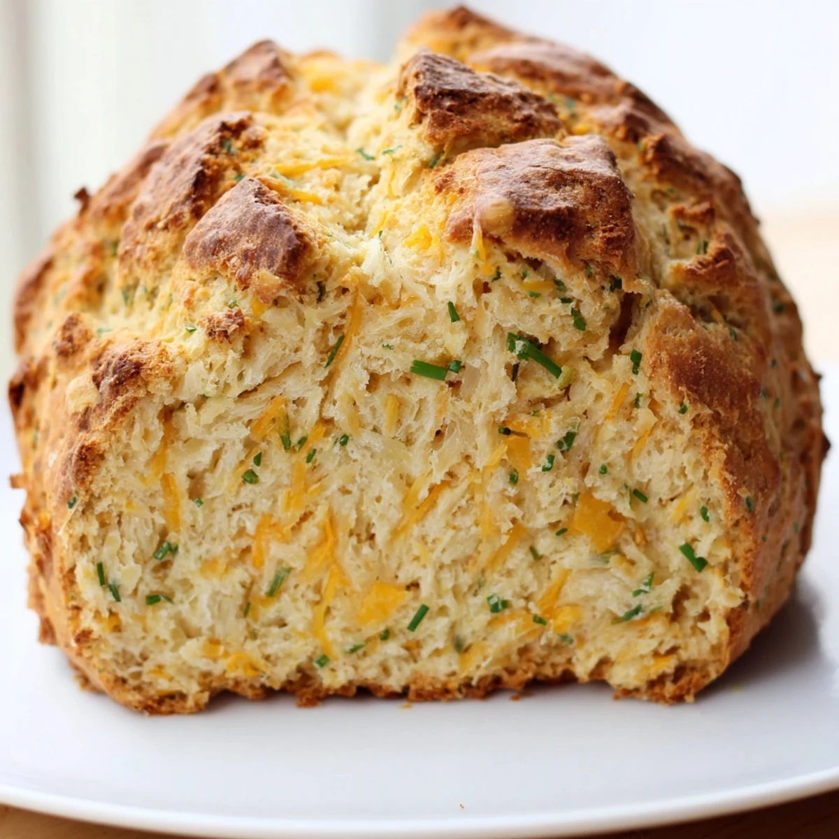 Freshly baked Savory Cheddar & Chive Irish Soda Bread on a cooling rack, with melted cheddar and chives visible on top.