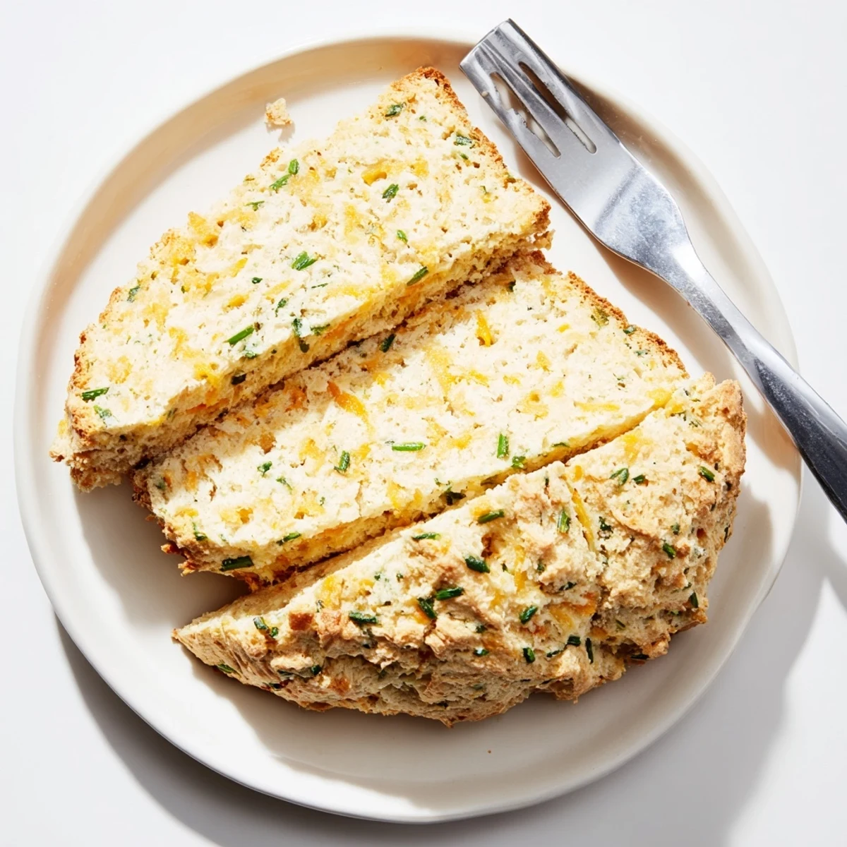 Slices of Savory Herbed Cheddar Irish Soda Bread are ready to serve beside a warm bowl of creamy soup.