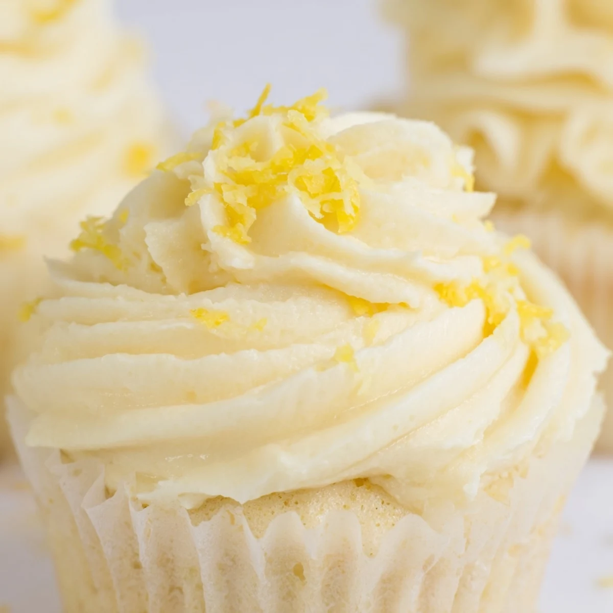 A close-up of frosted Limoncello Cupcakes reveals moist cake crumbs and glossy lemon glaze, arranged on a white ceramic plate.