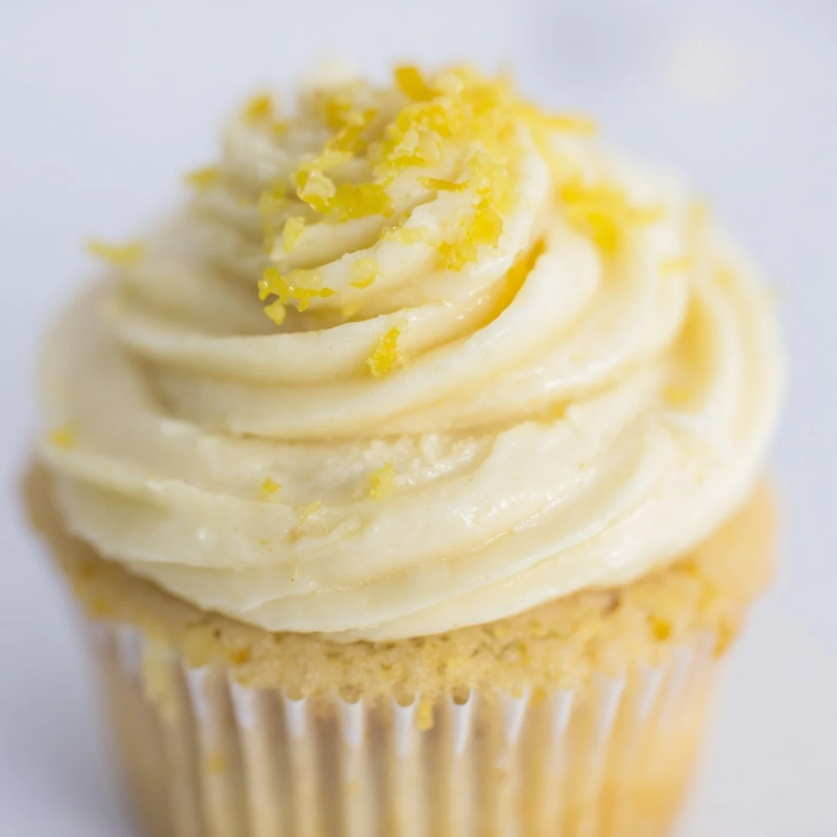 Twelve Limoncello Cupcakes sit in a muffin tin liner, topped with pale yellow buttercream and a light dusting of powdered sugar.