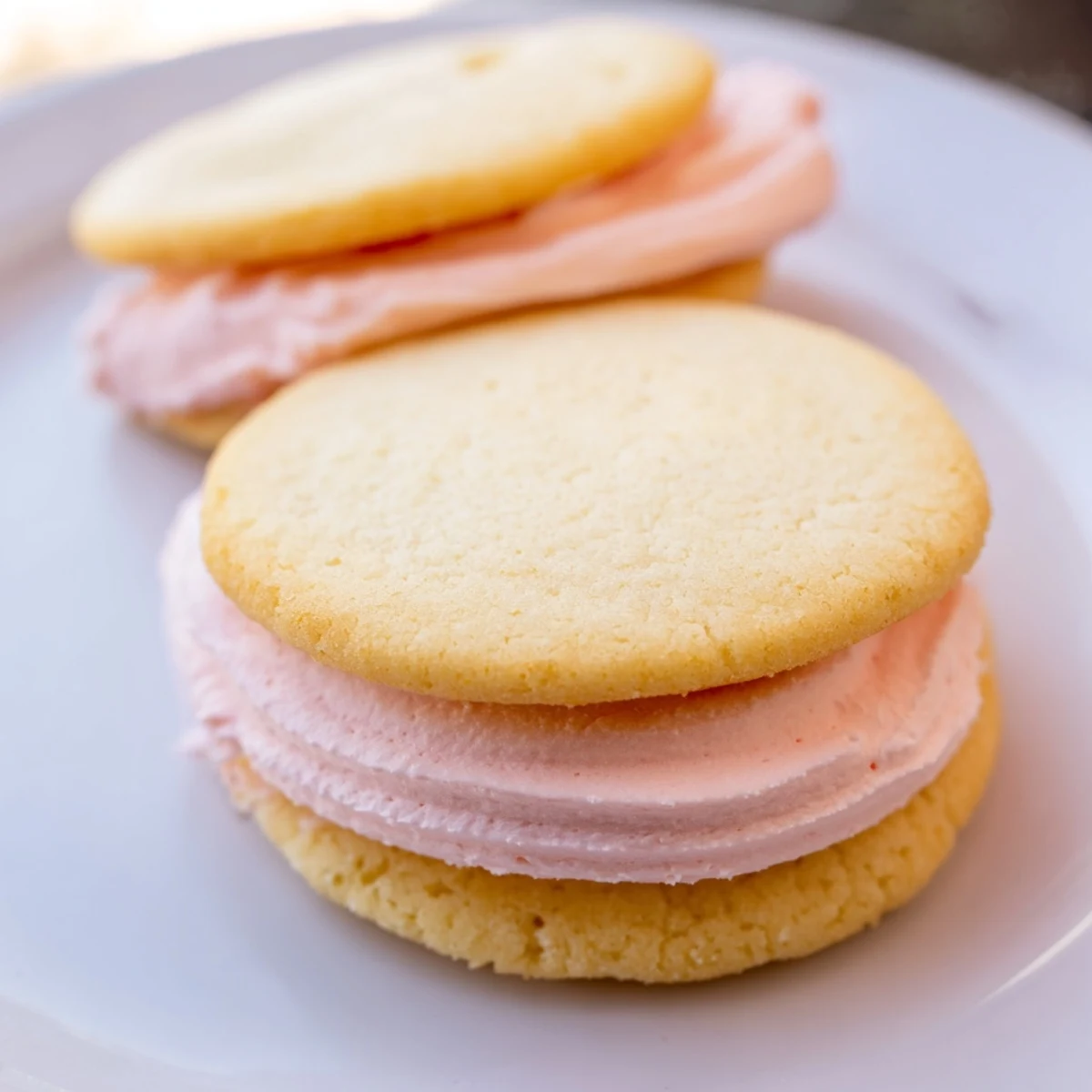 Stacked pastel sugar cookie sandwiches with pink and yellow buttercream, perfect for spring celebrations.