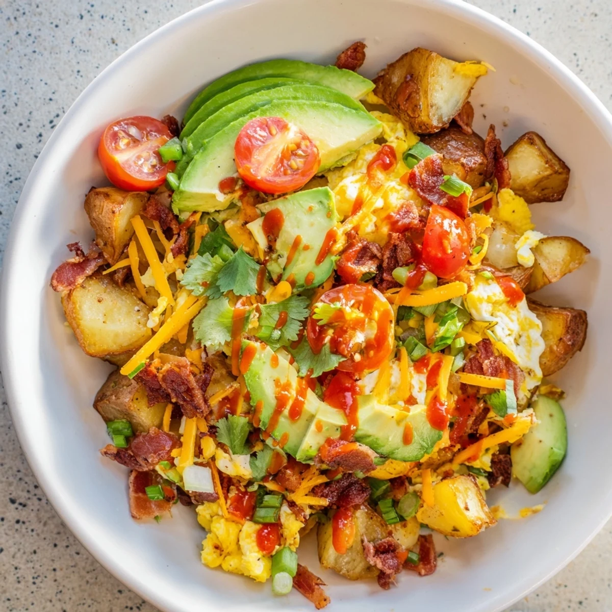 Enjoy a Loaded Breakfast Bowl with hearty potatoes, eggs, bacon, cheese, avocado, and fresh tomatoes, ready to serve for breakfast.
