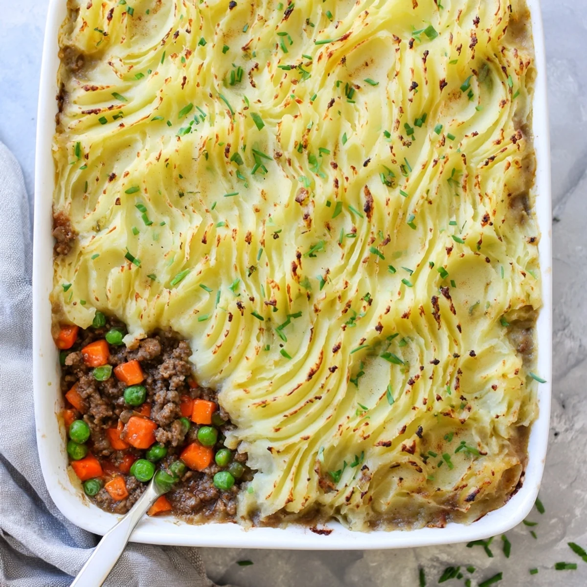 A hearty slice of Shepherd's Pie with Creamy Garlic Mashed Potatoes served on a white plate beside a glass of red wine.