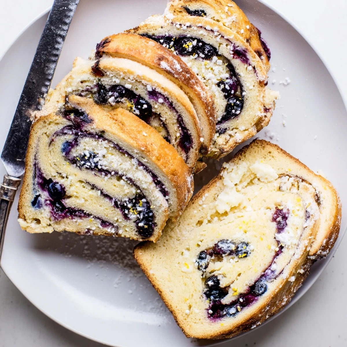 A sliced loaf of Blueberry Lemon Cream Cheese Sourdough showing the vibrant blueberry swirl and creamy cheese pockets on a wooden board.