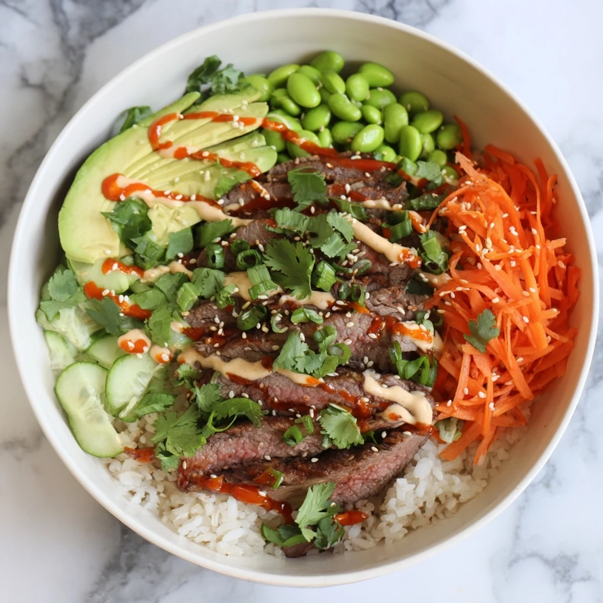 Sliced flank steak arranged over fluffy rice with colorful vegetables and spicy sriracha mayo drizzle