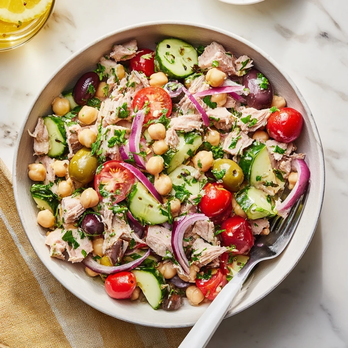 Rustic wooden table displaying hearty tuna and garbanzo bean salad topped with parsley and lemon wedges