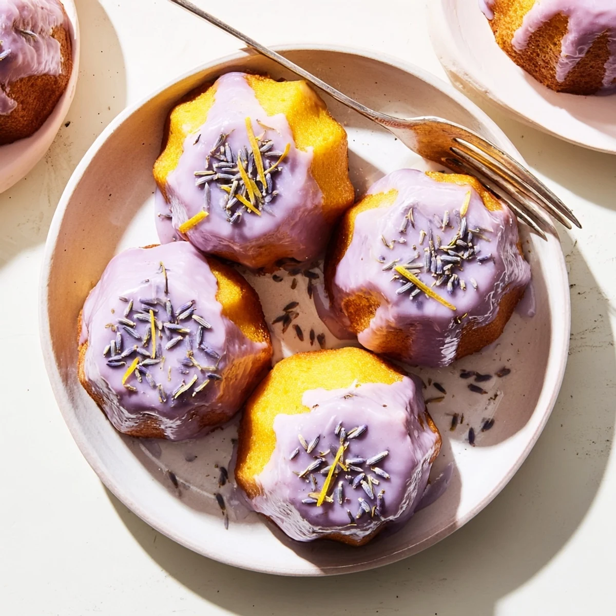 Moist lemon mini cakes topped with floral lavender icing on a white serving platter