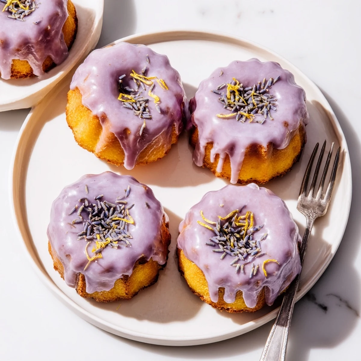 Elegant mini lemon cakes with smooth lavender glaze garnished with fresh lemon zest strips