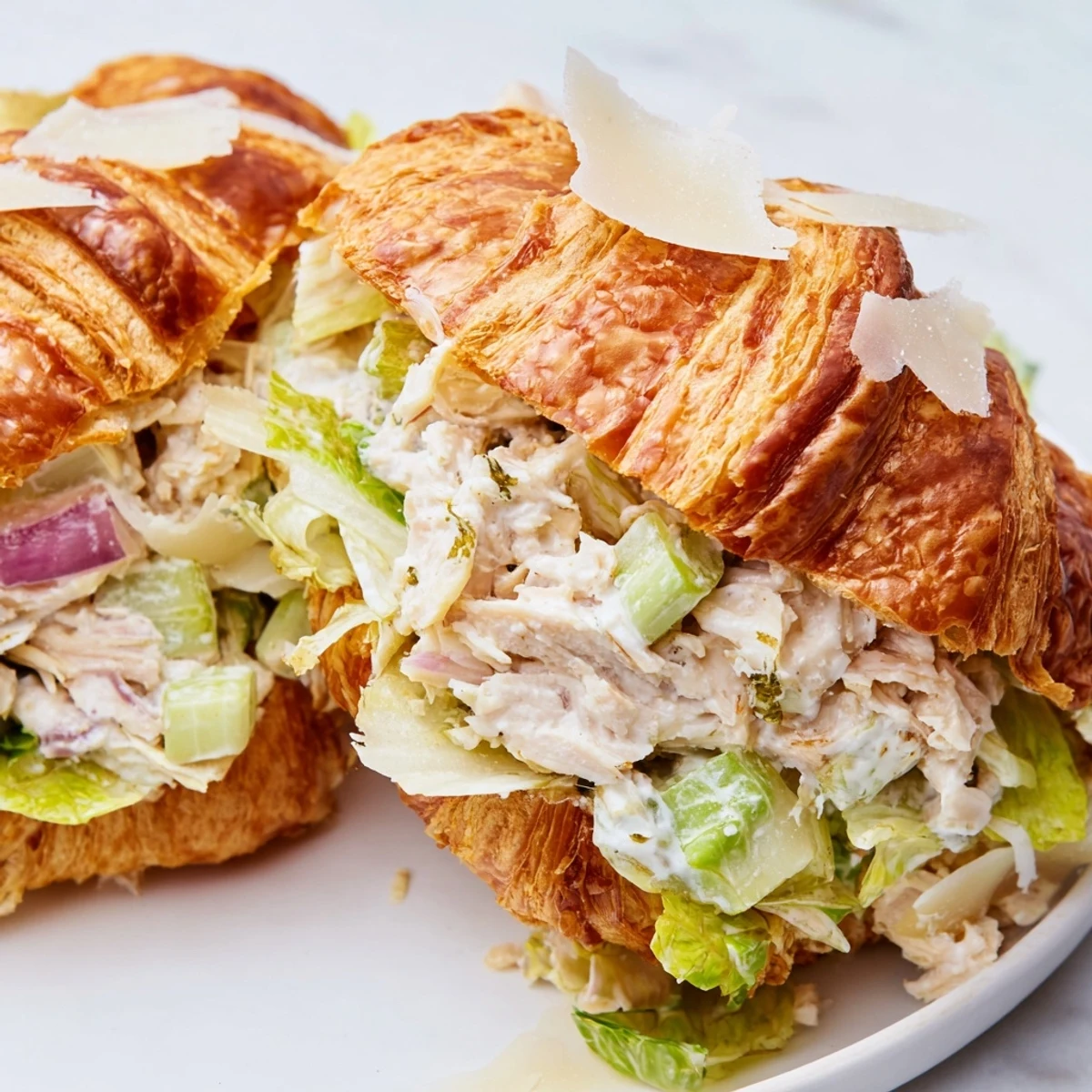 Sliced chicken Caesar salad croissant sandwich topped with grated Parmesan on wooden board
