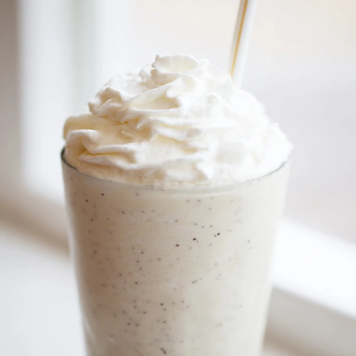 Garnished glass of vanilla bean frappuccino topped with fluffy whipped cream and vanilla specks