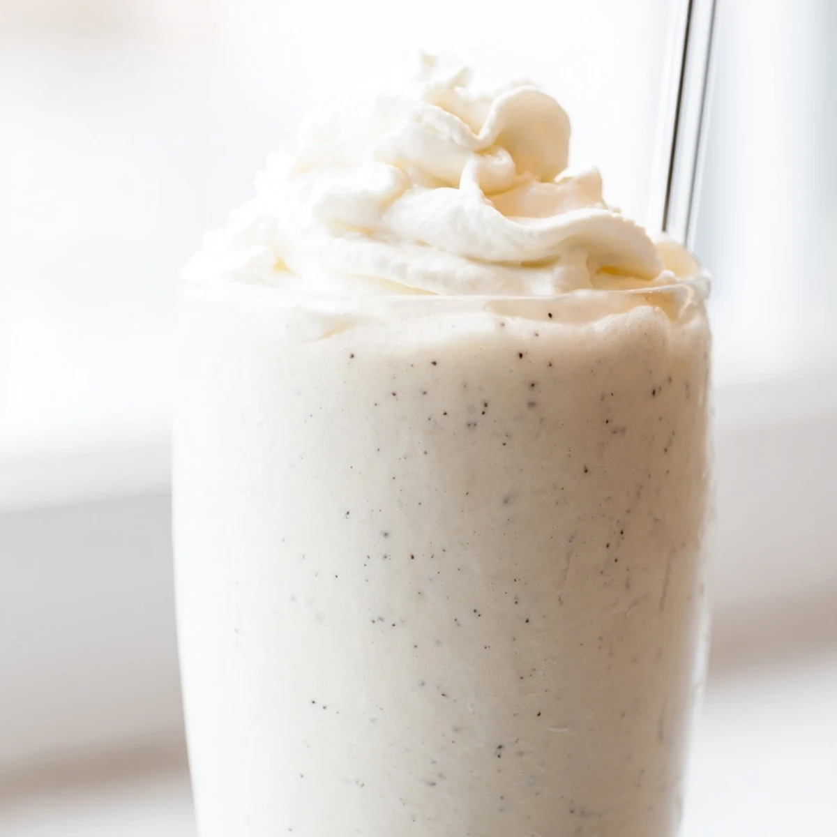 Tall chilled glass displaying creamy vanilla bean frappuccino with white chocolate shavings on top