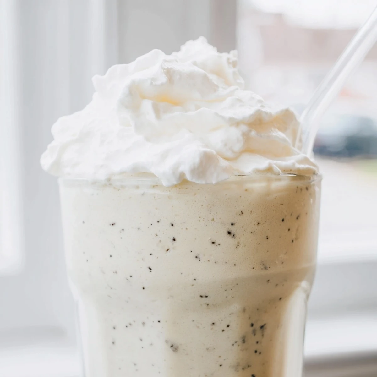 Two homemade vanilla bean frappuccinos served with straws and dollops of sweetened whipped cream