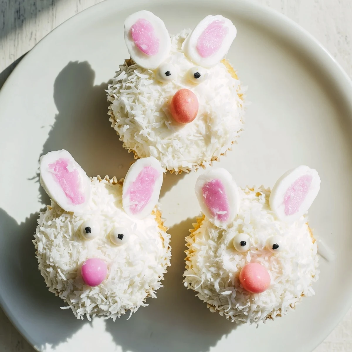 Adorable bunny cupcakes topped with fluffy coconut fur, pink marshmallow ears, and candy eyes for Easter