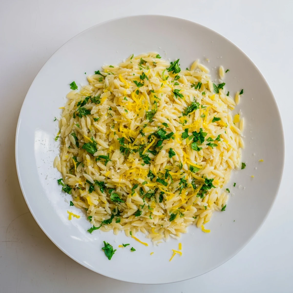 Golden lemon orzo pasta flecked with fresh parsley and grated Parmesan cheese in a white serving bowl