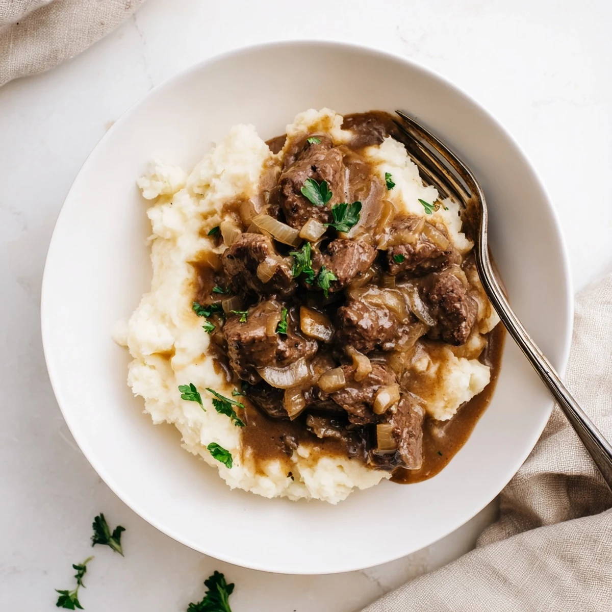 Tender slow cooker beef tips and gravy served over creamy mashed potatoes with fresh parsley garnish