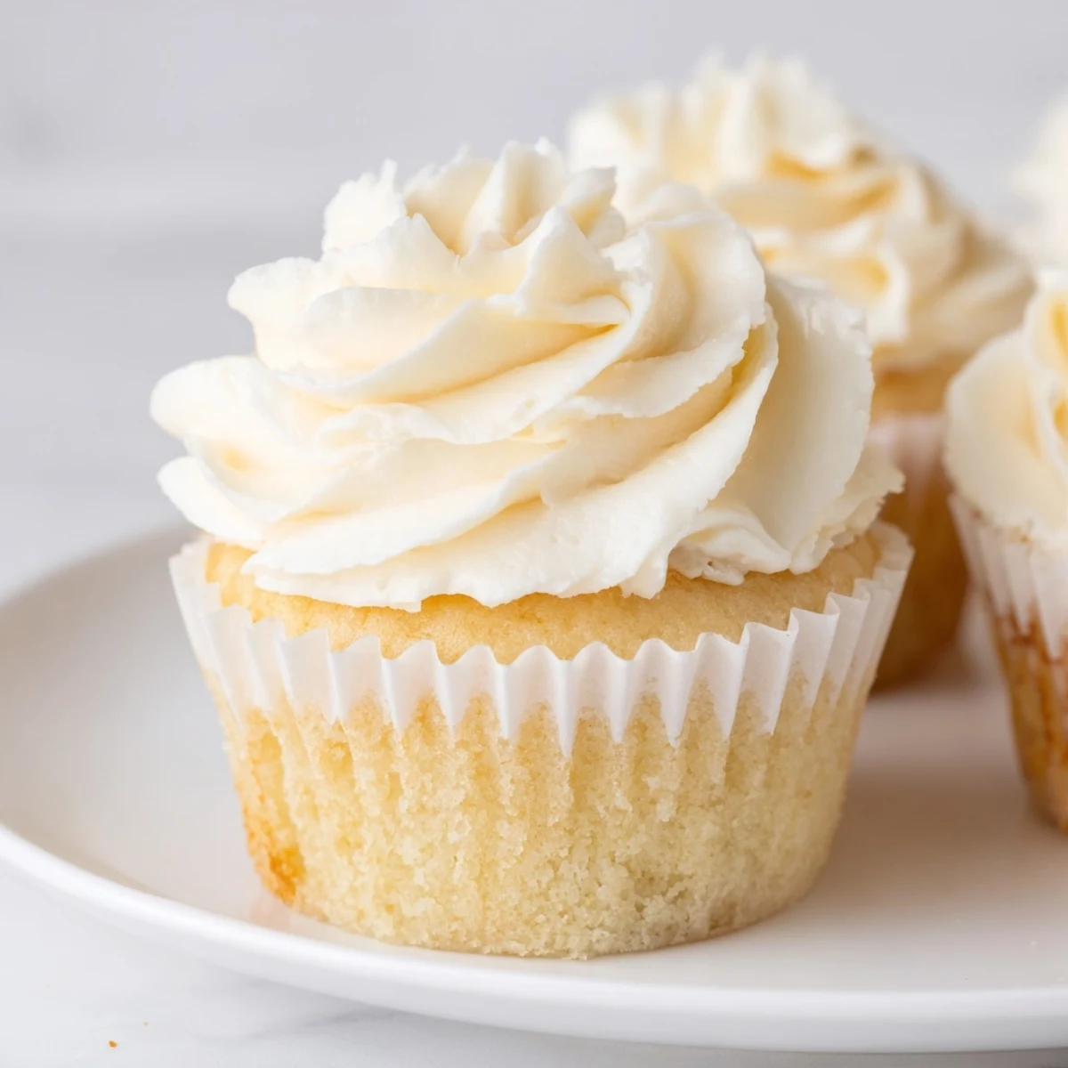 Fluffy vanilla cupcakes topped with swirls of creamy vanilla buttercream frosting on a white plate