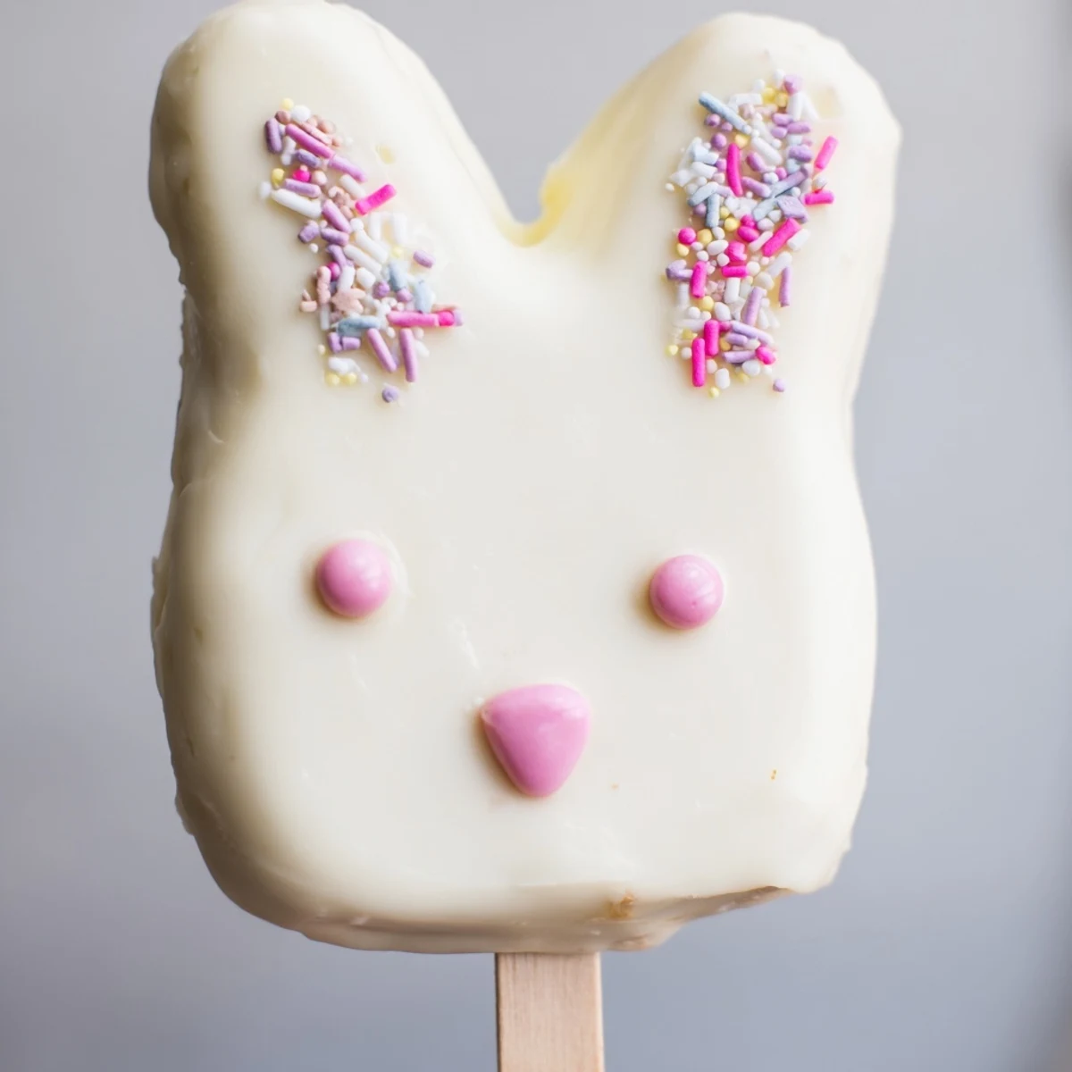 Adorable white chocolate bunny cakesicles with candy eyes on a wooden serving board