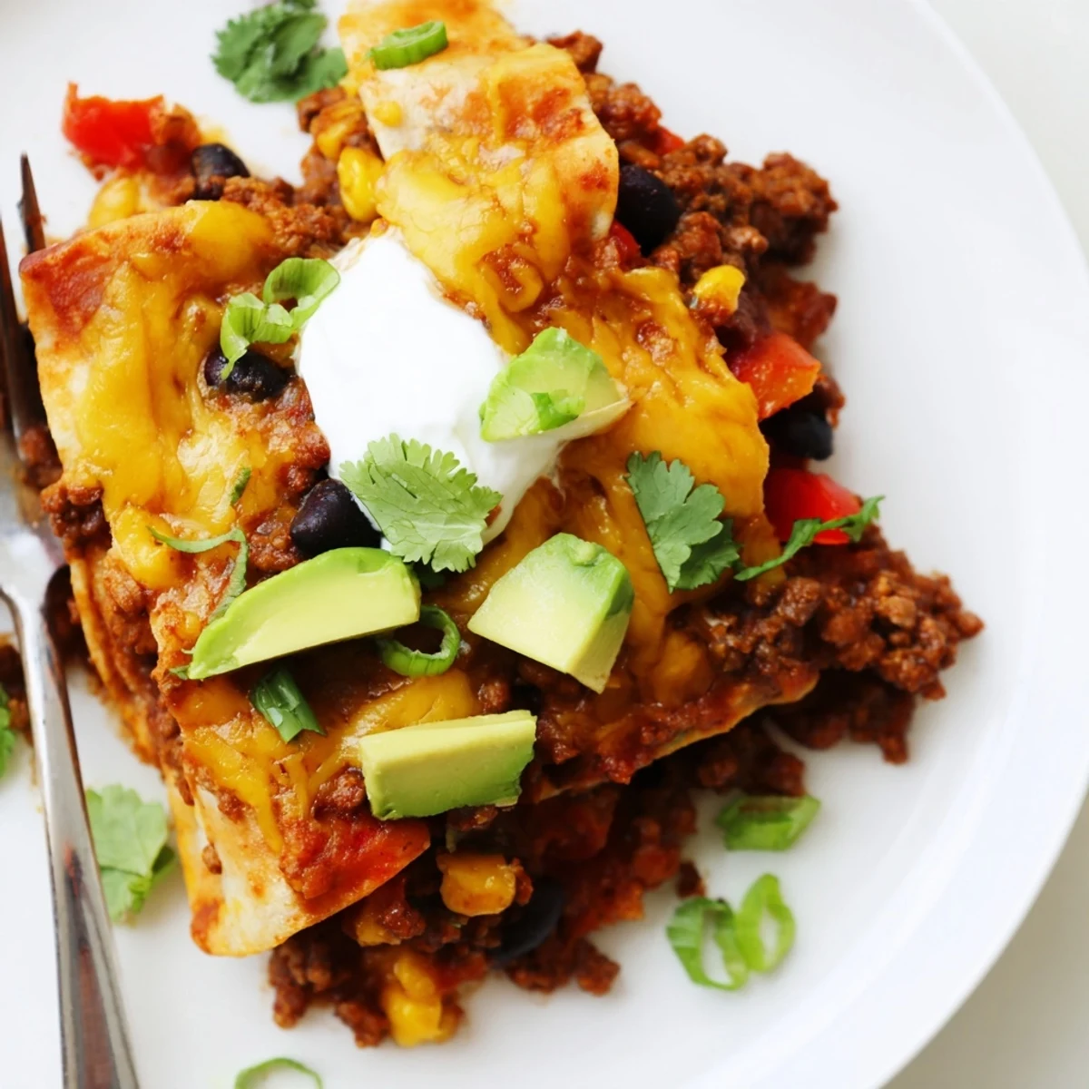 Warm Beef Skillet Enchiladas topped with cilantro, sour cream, and diced avocado